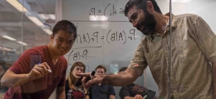 Statistics Professor Andrew Schaffner works with a student writing equations on glass walls