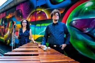 Bass clarinetist Amy Advocat and marimbist Matt Sharrock of Transient Canvas stand with instruments in front of a colorful mural