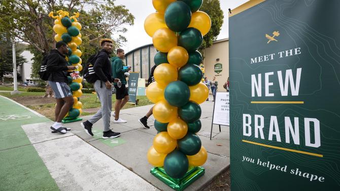 A sign stating "New Brand" sits next to a display of green and gold balloons. 