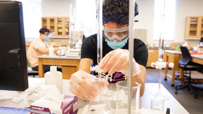 Students fiddles with a test tube and watches a reaction during a chemistry lab