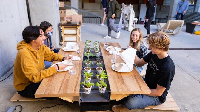 Students sit around a table that was created for the Vellum Furniture Design Competition. 