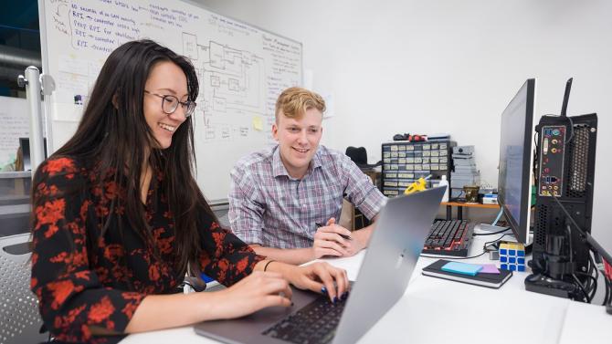 Two CIE students collaborate on their project together, using a computer