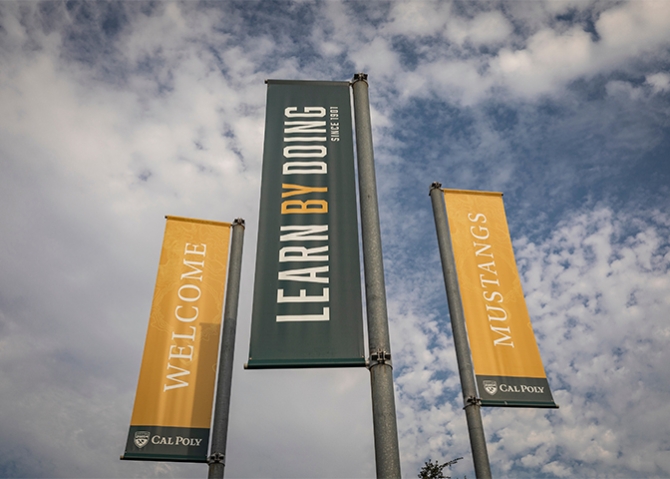 A trio of campus entrance banners say Welcome, Mustangs, and Learn by Doing -- Since 1901